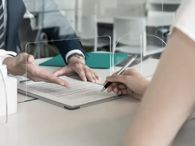 Dos personas firman un contrato en el mostrador de una oficina bancaria